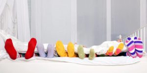 Happy family concept. Feet of father mother and four children in colorful knitted socks on white bed. Family sleeping together.