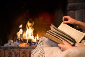 hands of woman reading book by fireplace